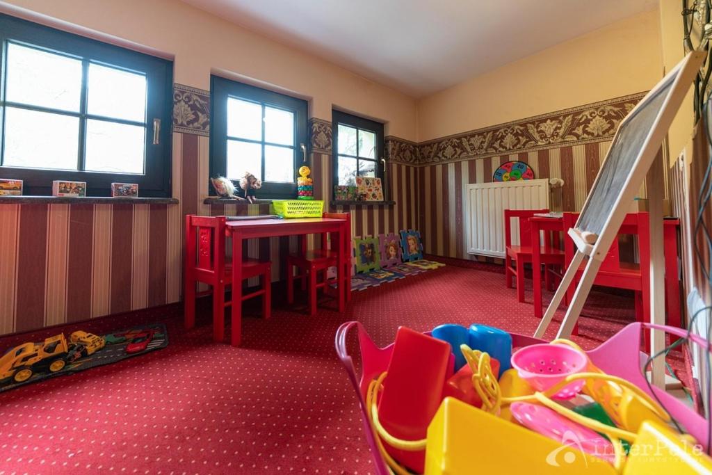 Children's playroom with red tables and chairs, toys on floor and three windows lighting room.