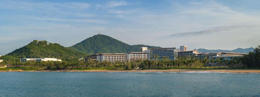 un groupe de bâtiments sur une plage avec des montagnes en arrière-plan dans l'établissement Hyatt Regency Sanya Tianli Bay, à Sanya
