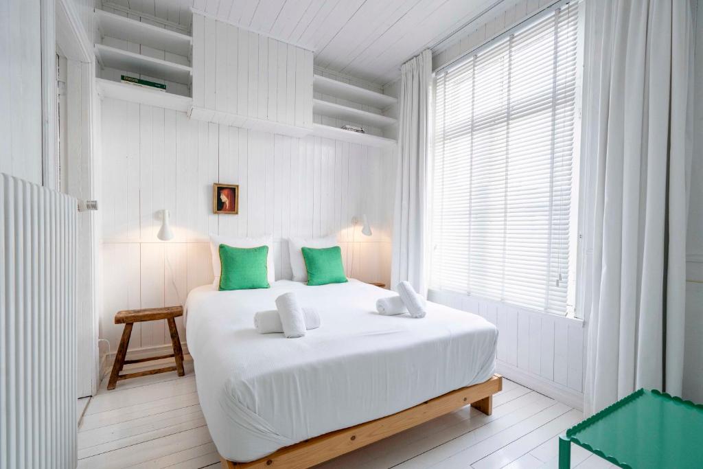 um quarto branco com uma grande cama branca com almofadas verdes em The Handshake House em Antuérpia