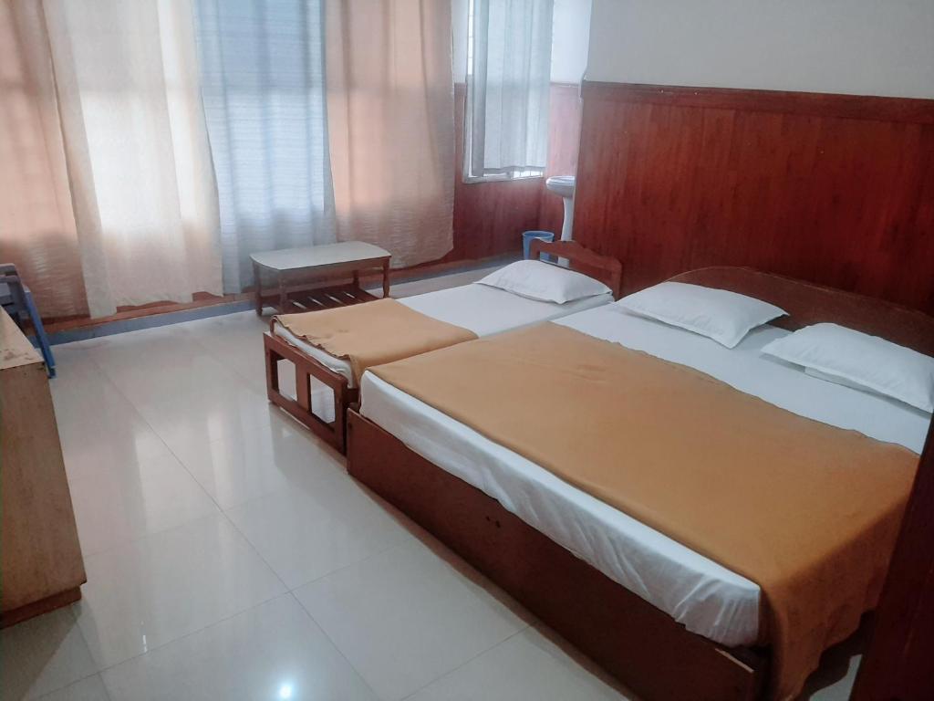 1 dormitorio con 2 camas, mesa y ventanas en Budget comfort en Madikeri