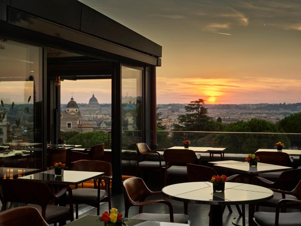 een restaurant met tafels en stoelen en een zonsondergang bij Hotel Eden - Dorchester Collection in Rome