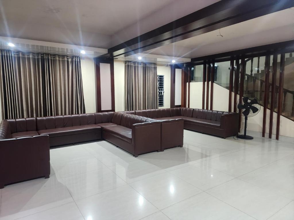 - un salon avec des canapés en cuir brun et des fenêtres dans l'établissement Urmee Guest House, à Cox's Bazar