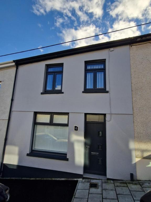 a white house with a black door and windows at Comfortable 3 Bed home Merthyr Tydfil near Bike Park Wales & Brecon Beacons in Dowlais