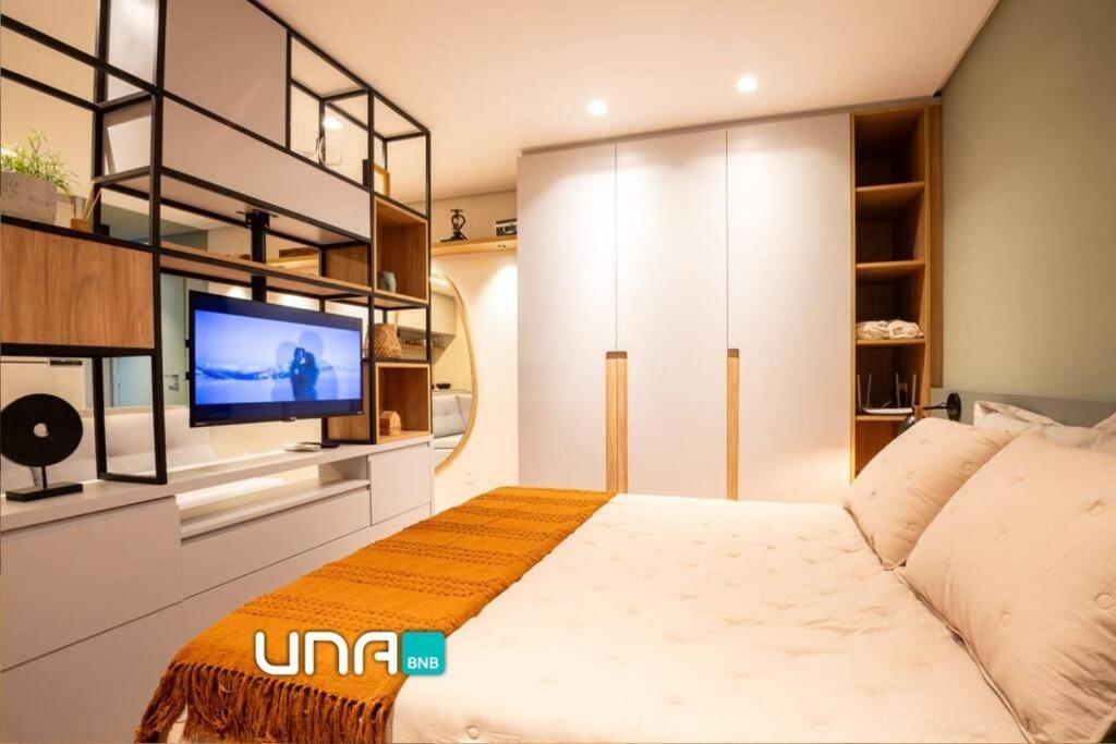 1 dormitorio con 1 cama y TV en la pared en Studio 506 com vista Parque Una, en Pelotas