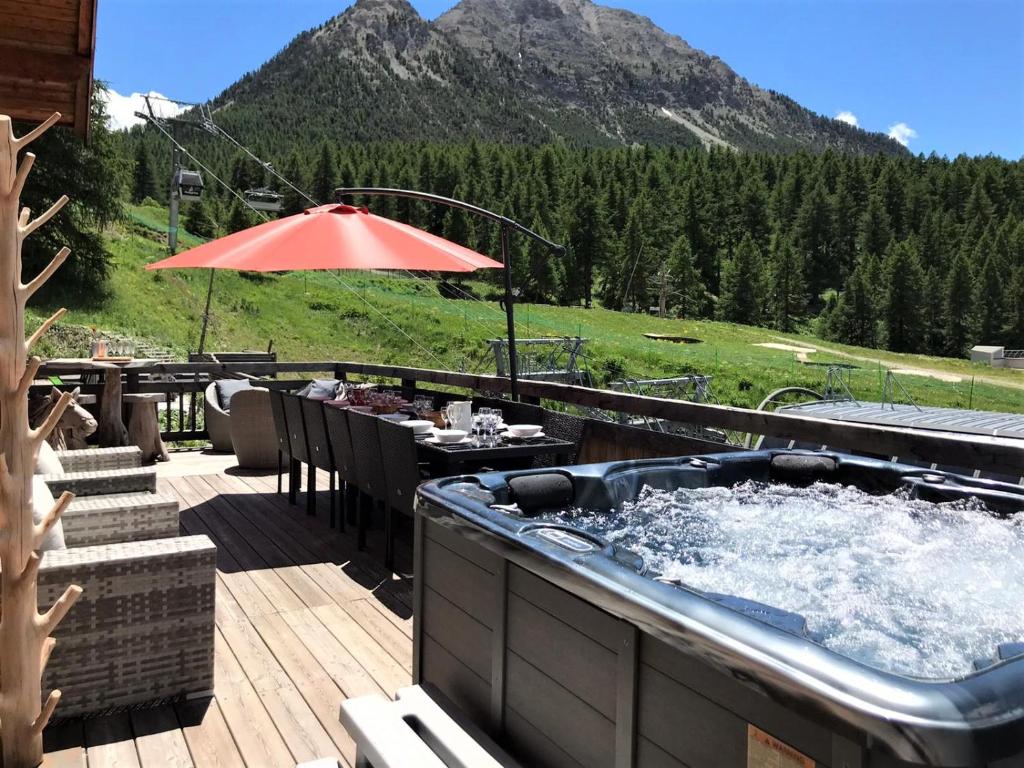 a hot tub on a deck with a table and an umbrella at Slope-Side Chalet w/Jacuzzi, Home Cinema, for 16 Guests in Montgenèvre