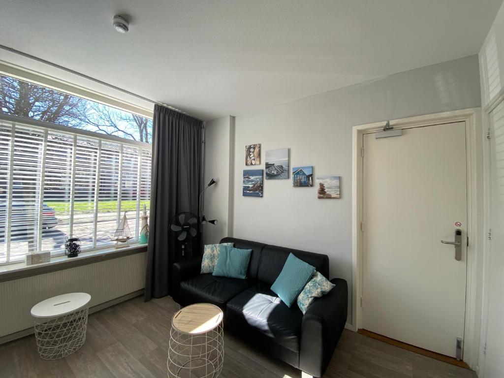 a living room with a black couch and a window at De Zeekreeft in Katwijk aan Zee