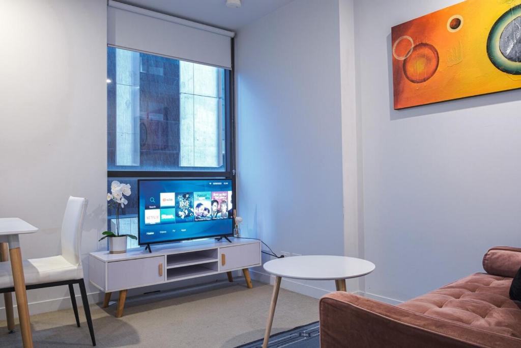ein Wohnzimmer mit einem TV, einem Sofa und einem Fenster in der Unterkunft Relaxing 1br1ba Apartment In Melbourne Cbd in Melbourne