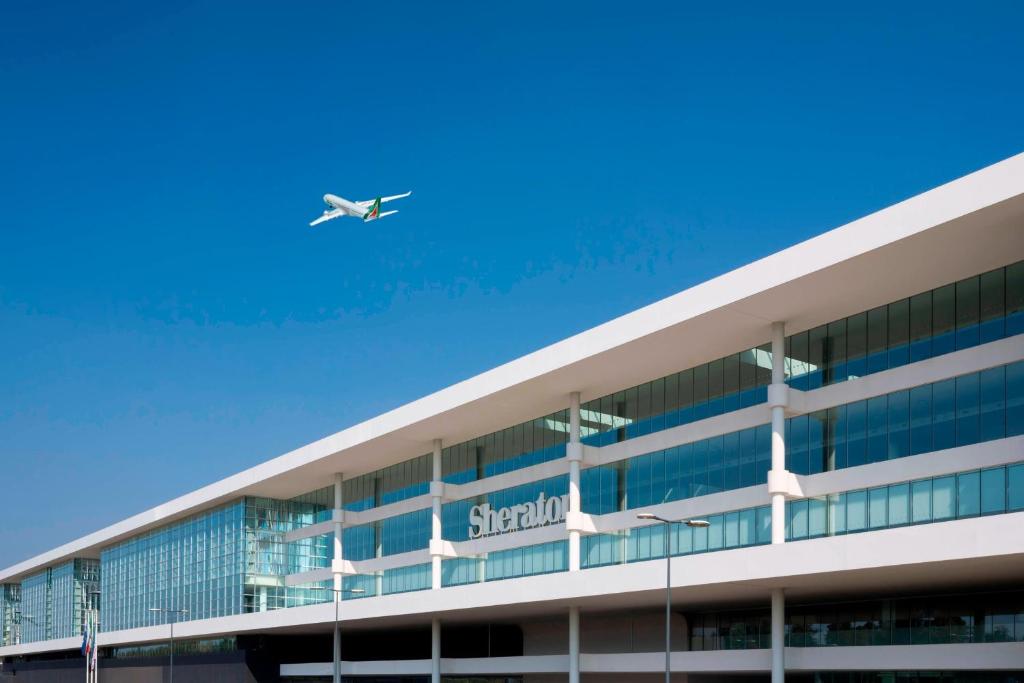 un avion survolant un bâtiment avec un aéroport dans l'établissement Sheraton Milan Malpensa Airport Hotel & Conference Centre, à Ferno