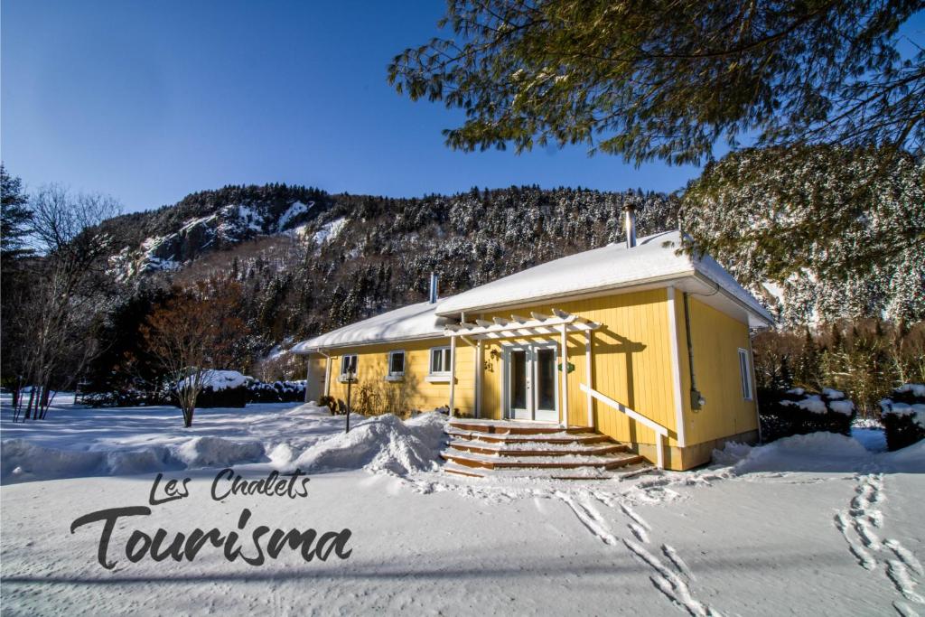 mały żółty budynek w śniegu z górą w obiekcie Les Chalets Tourisma - Chalet au bord de l'eau avec spa et foyer - Le Draveur w mieście Saint-Raymond