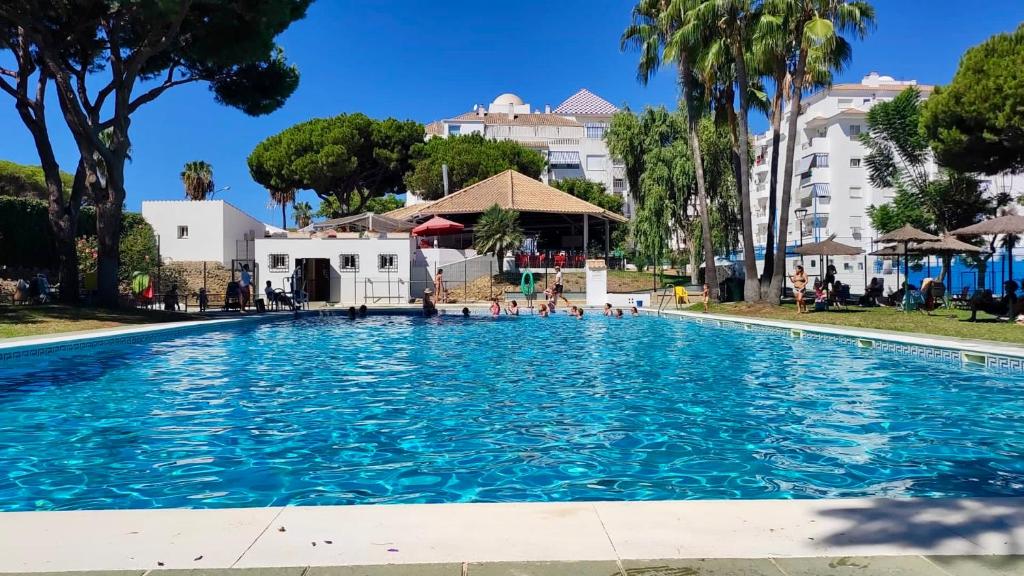 uma piscina num resort com palmeiras e edifícios em Apartamento Pinares del Portil a pie de playa em El Portil
