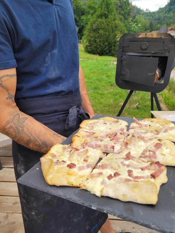 a man holding a large pizza on a table at Gîte de la Ferme de la Comté in Le Thillot