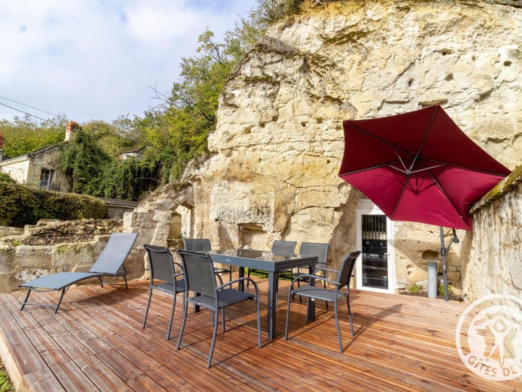 a table with chairs and a red umbrella on a wooden deck at Gîte troglodyte unique avec jacuzzi, billard et jardin, près de Doué La Fontaine et Saumur - FR-1-622-69 in Les Ulmes