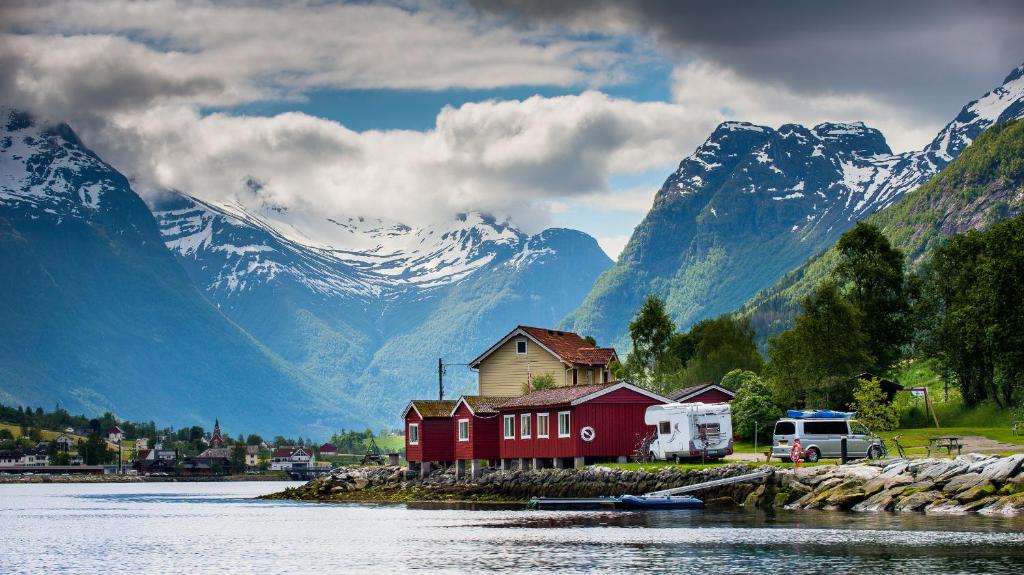 a house on a island next to a river with mountains at Nesset Fjordcamping in Olden