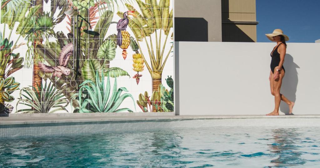 Eine Frau, die neben einer Wand steht, mit einem Wandbild aus Pflanzen in der Unterkunft Essence Peregian Beach Resort - Lily 4 Bedroom Luxury Home with Private Pool in Peregian Beach