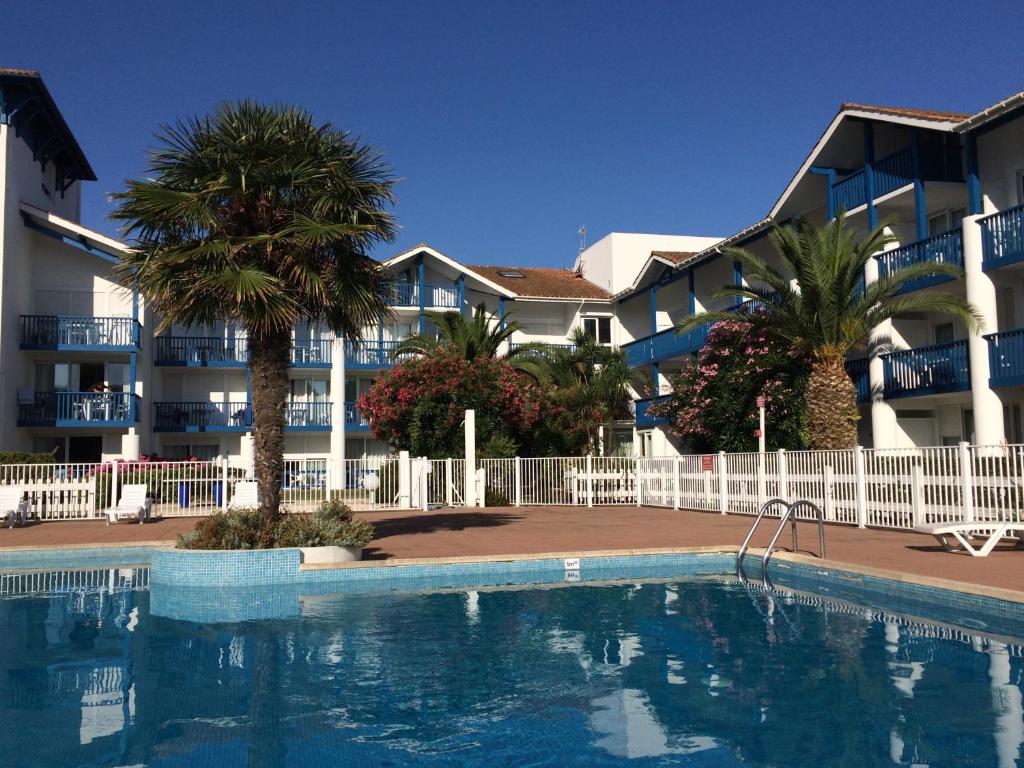 - une piscine en face d'un bâtiment avec des palmiers dans l'établissement Résidence Mer & Golf Fort Socoa, à Urrugne