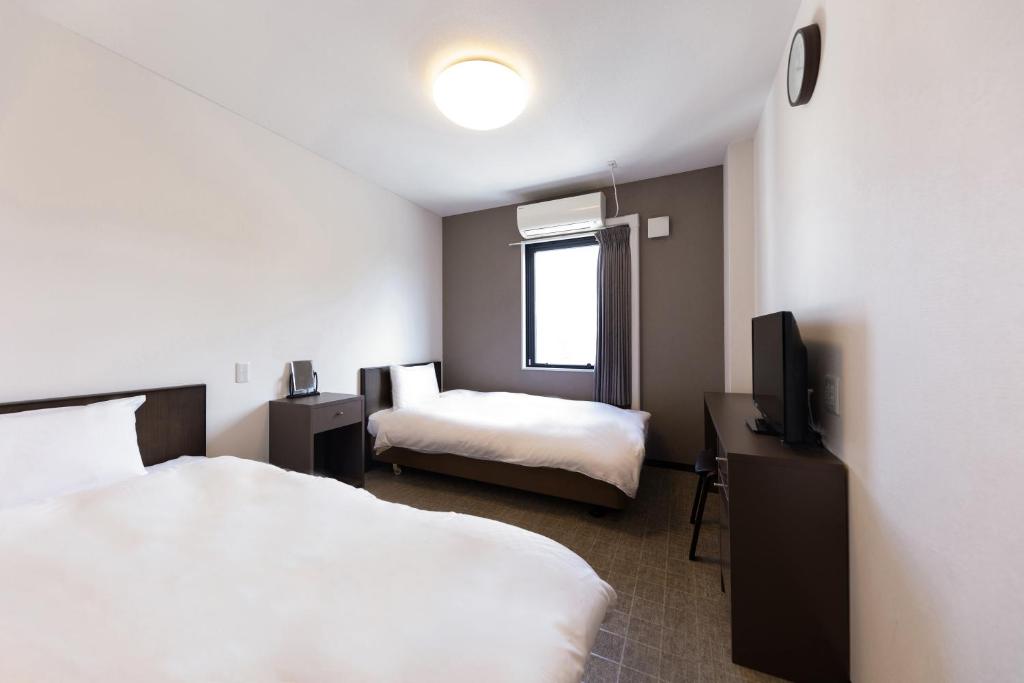 大阪市にあるOKINI HOTEL nambaのベッド2台とテレビが備わるホテルルームです。