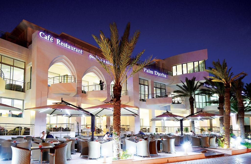 a building with tables and umbrellas in front of it at Palm Djerba Suites in Mezraya