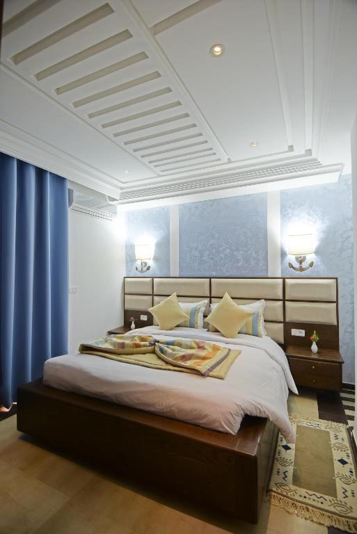 a bedroom with a large bed with blue curtains at Palm Djerba Suites in Mezraya