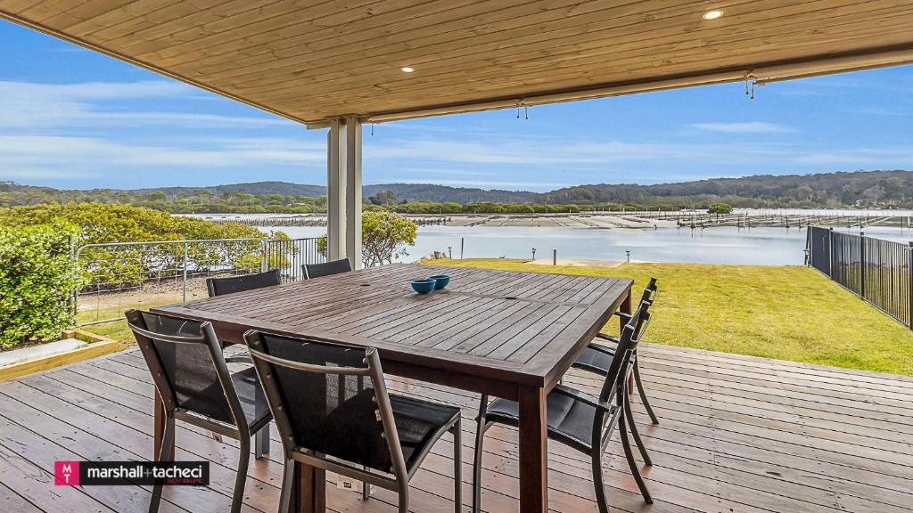 a wooden table and chairs on a deck with a view of the water at Bermagui River View - Unit 1,1 Lindo Street 3 bdrm Villa in Bermagui