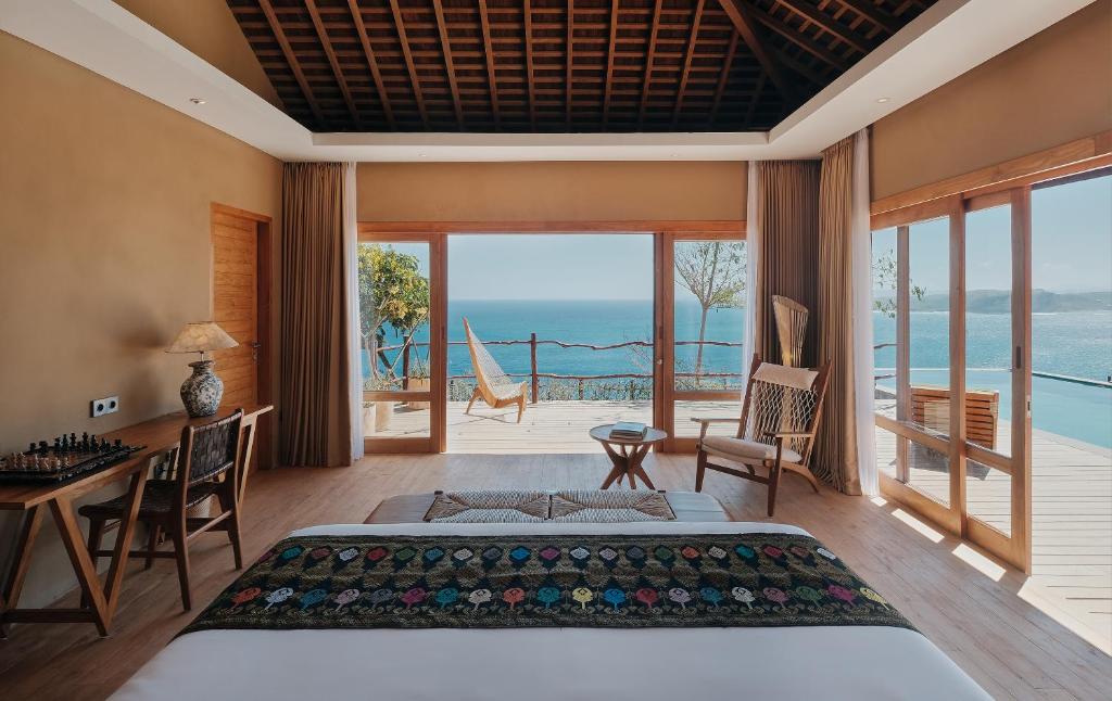 a bedroom with a bed and a desk with a view of the ocean at TUNAK Resort Lombok in Bumbang