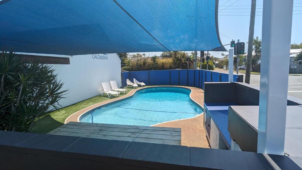 uma piscina com cadeiras e um guarda-sol azul em Moffat Beach Motel Caloundra em Caloundra