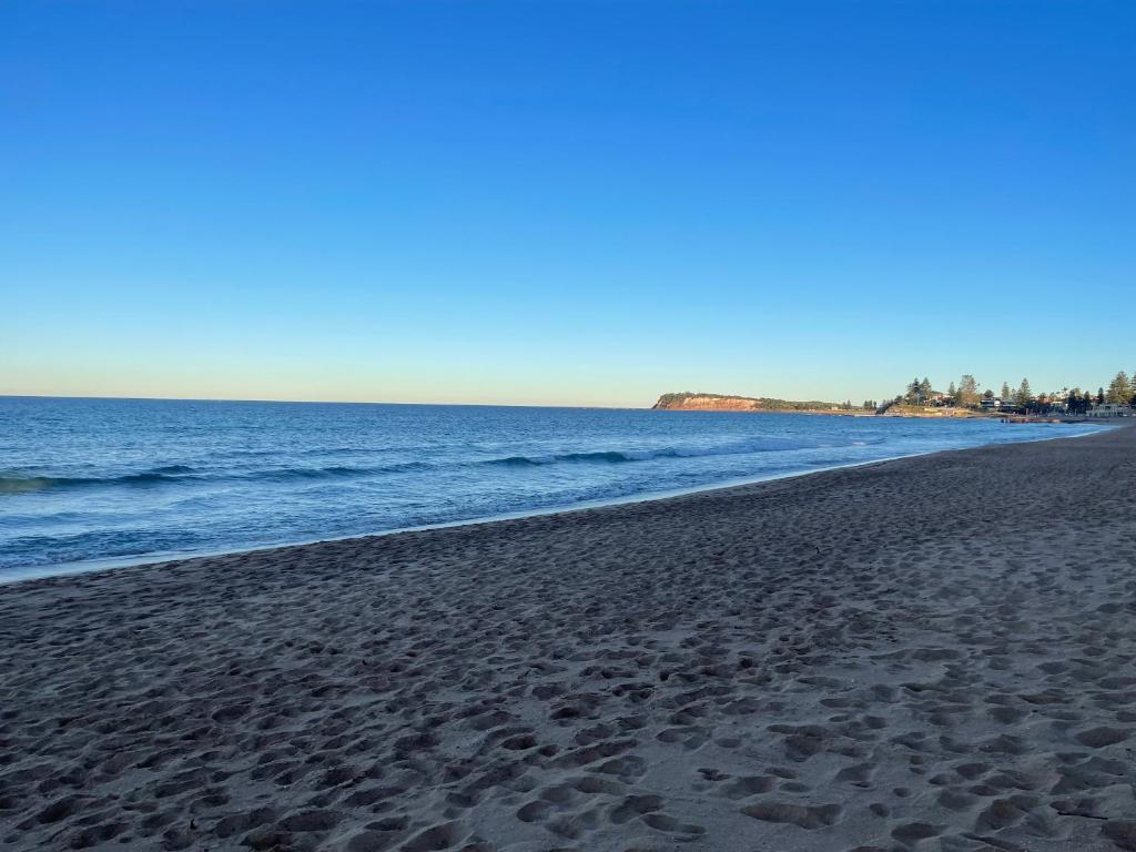 a beach with footprints in the sand and the ocean at Plateau Of The Seas in Collaroy