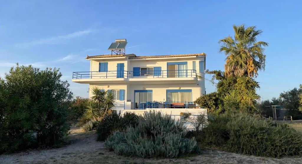 a white house with a balcony and a palm tree at Villa Caretta - direkt an einem einsamen Strand im Süden des Peloponnes 