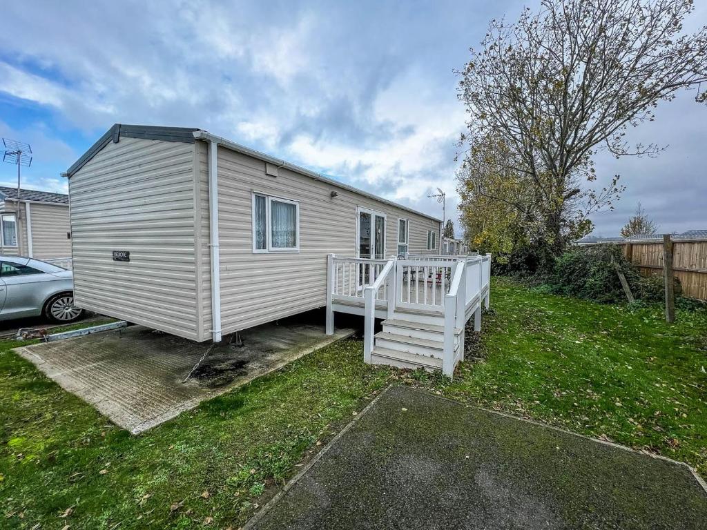 ein weißes winziges Haus mit einer Veranda und einem Auto in der Unterkunft Superb 6 Berth Caravan With Decking At Seawick Holiday Park, Essex Ref 27009mv in Clacton-on-Sea