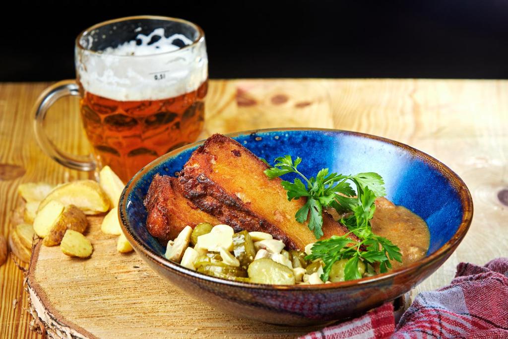 Rustic bowl of fried breaded pieces with pickled vegetables, potato wedges and a frothy beer mug on wooden board.