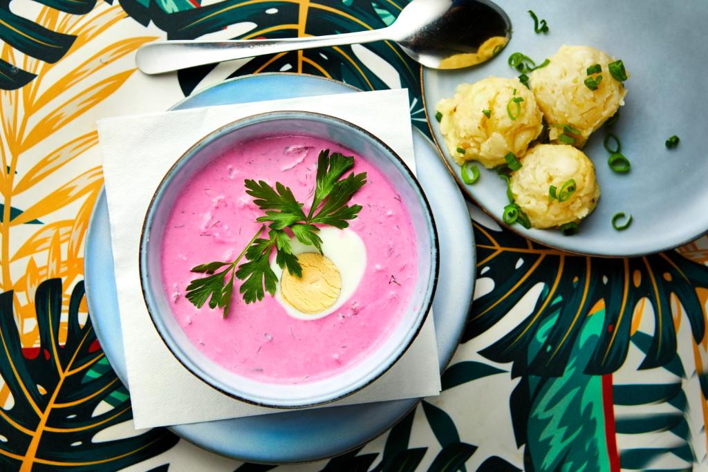 Bowl of vibrant pink chilled soup garnished with half a boiled egg and parsley, served with potato dumplings.
