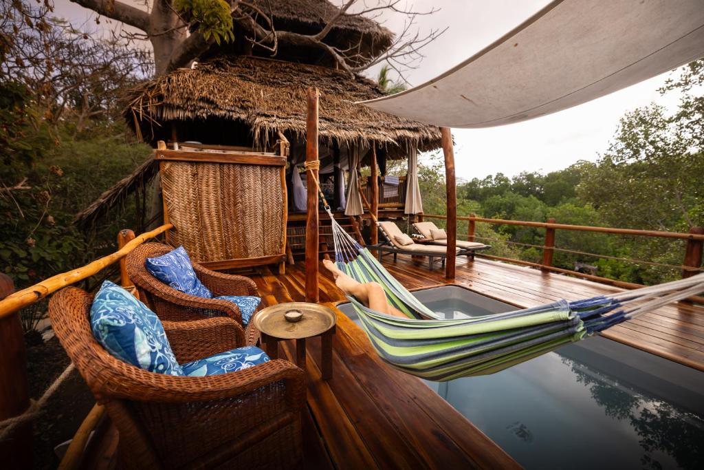a hammock and chairs on a deck with water at Chole Mjini Treehouses Lodge in Utende
