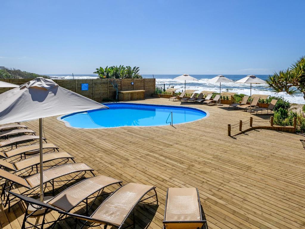 a swimming pool with chairs and an umbrella at Margate Beach Club in Margate