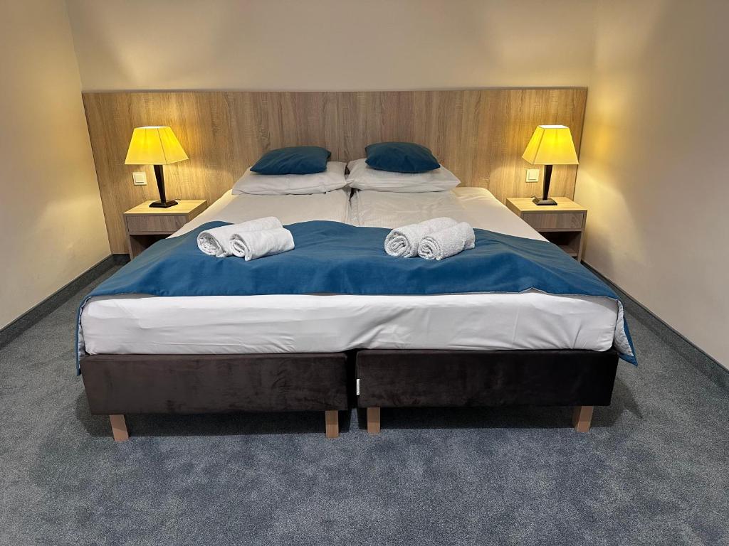 Neat double bed with blue runner, two rolled towels and warm bedside lamps in cozy room.