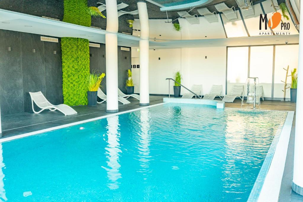 een zwembad in een gebouw met witte stoelen en een zwembad bij Westin House Resort by MS Pro in Kołobrzeg