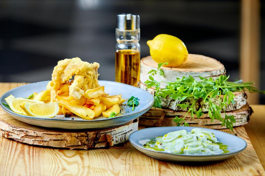 Plate of battered fish and fries with lemon wedges, oil bottle and fresh herb garnish.