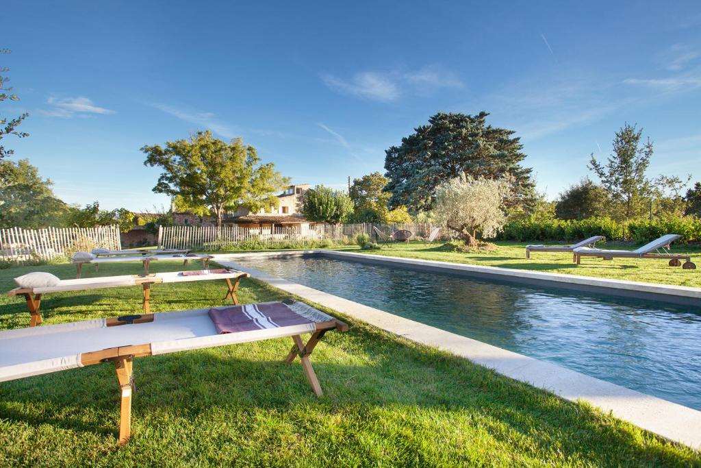 uma piscina de água com dois bancos na relva em Domaine Les Petites Vaines em Goult