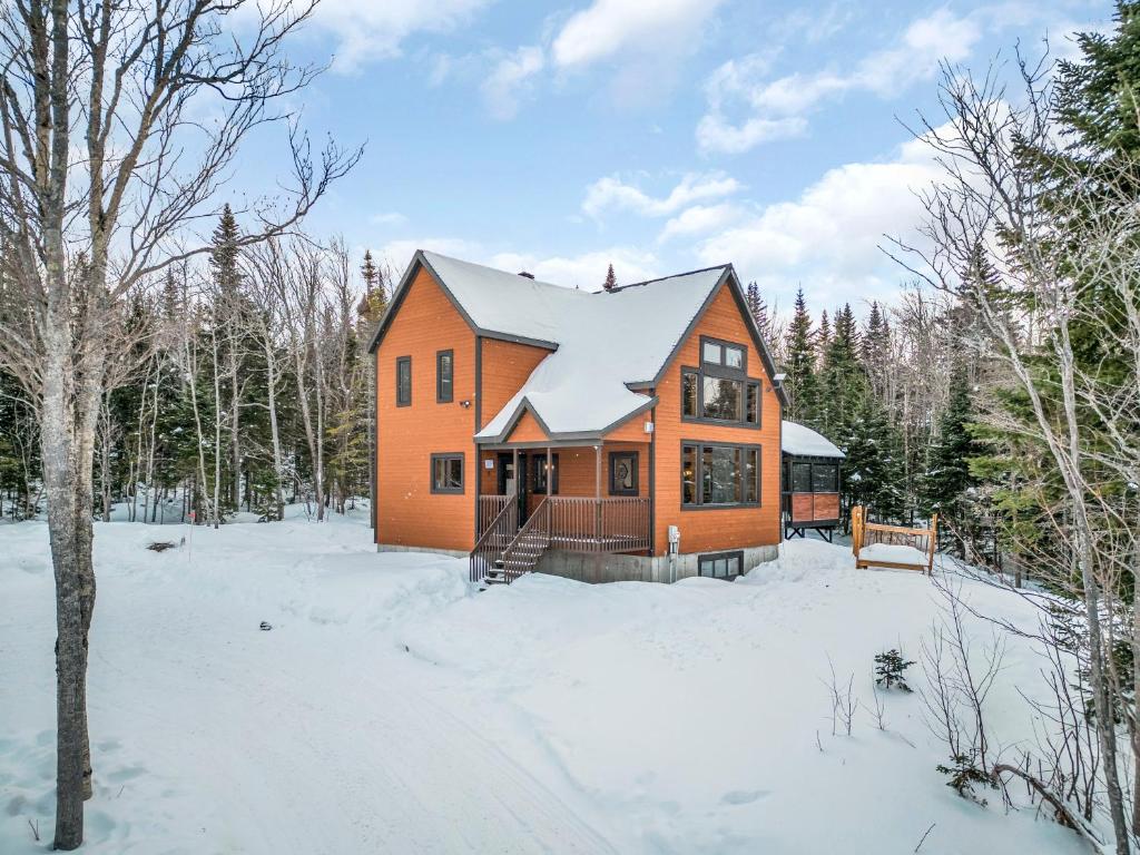 an orange house in the snow in the woods at Alpha Ö - Chalet Spa et detente in Petite-Rivière-Saint-François