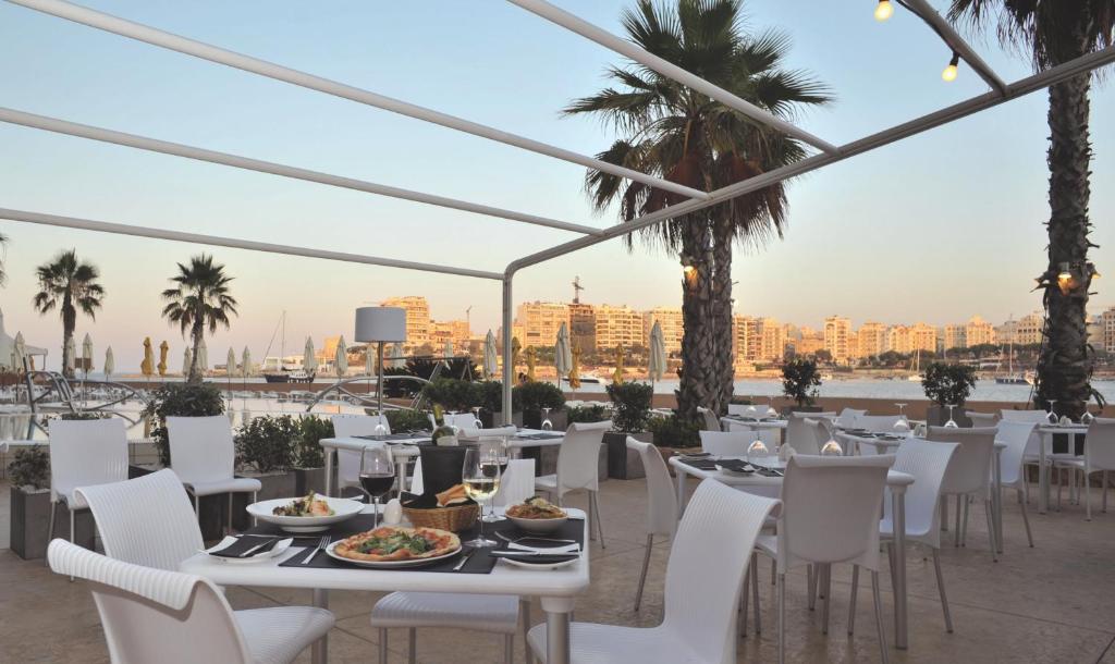 a restaurant with white tables and chairs and a view of the city at Cavalieri Art Hotel in St. Julianʼs