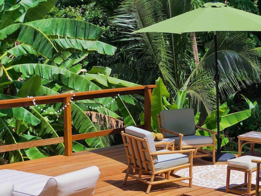 a deck with two chairs and a green umbrella at Little Diamond, Wooden Jungle House. Bathsheba. in Saint Joseph