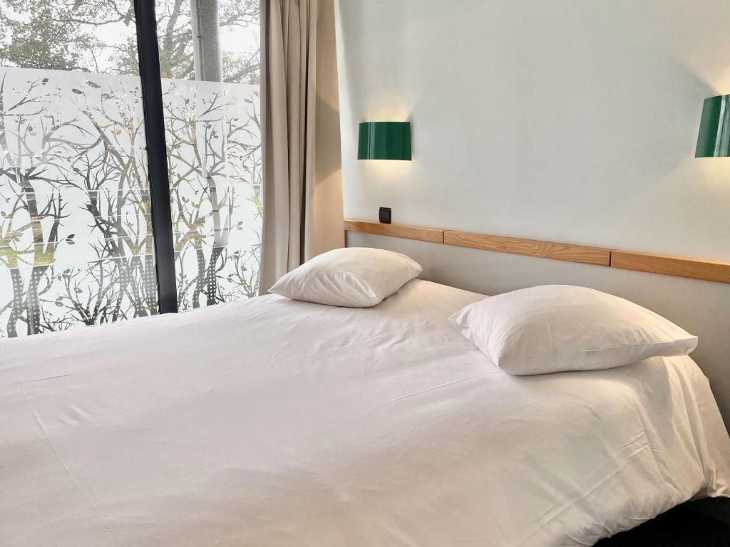 - un lit avec deux oreillers dans une chambre dotée d'une fenêtre dans l'établissement Le Keréden - Breizh Ecolodge Hôtel, à Locarn