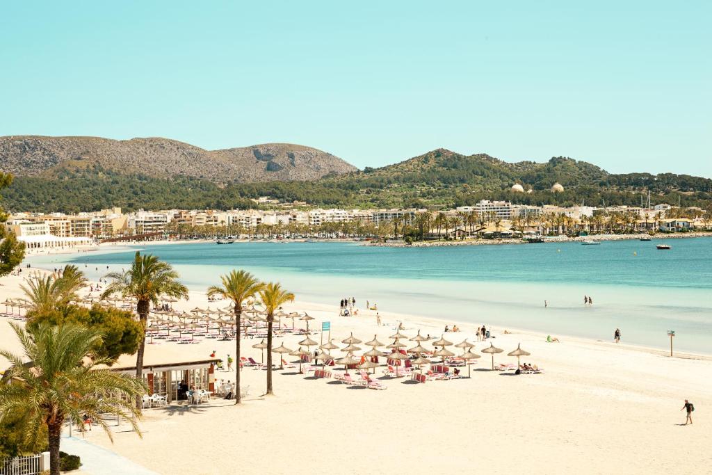 a beach with umbrellas and people on the beach at Sunwing Alcudia Beach in Alcudia