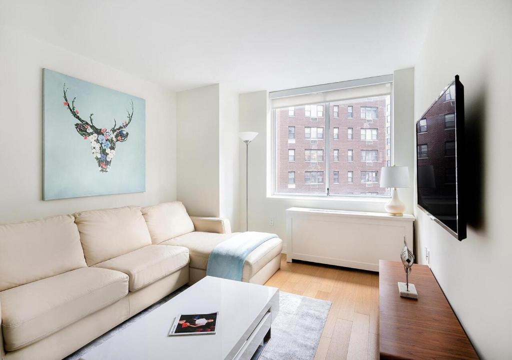 Stunning 2 BED 2 BA At UES في نيويورك: غرفة معيشة مع أريكة بيضاء ونافذة