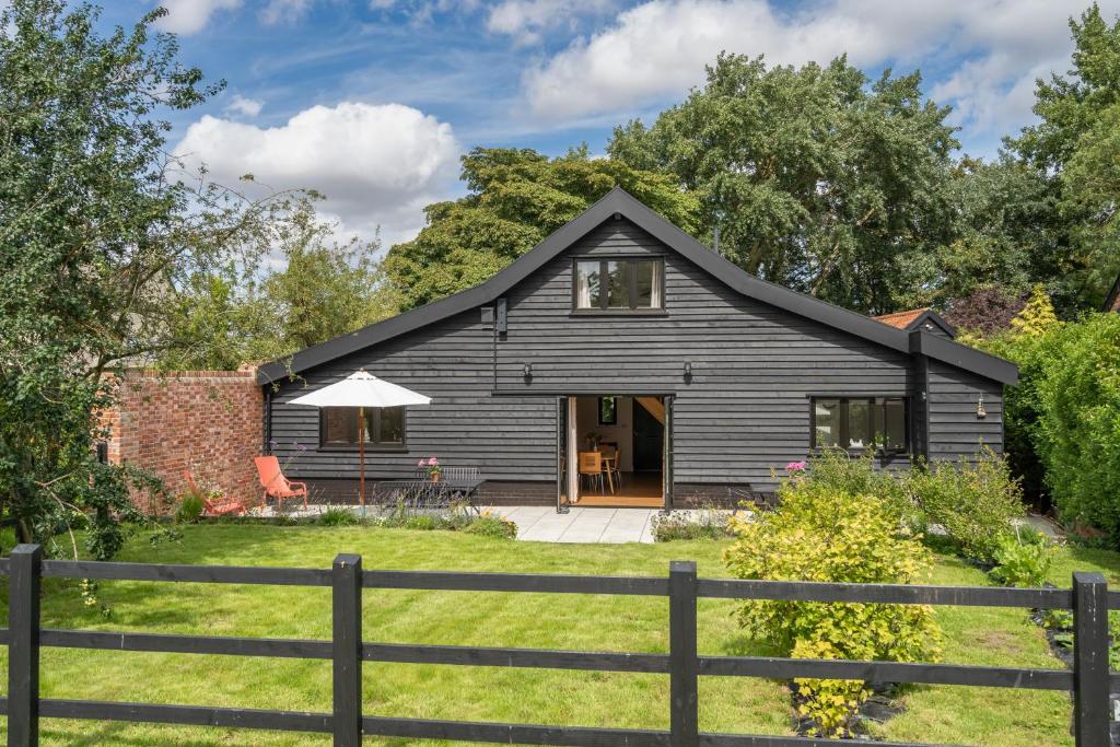 Ein schwarzes Haus mit einem Zaun davor. in der Unterkunft Contemporary Barn Waveney Valley in Harleston