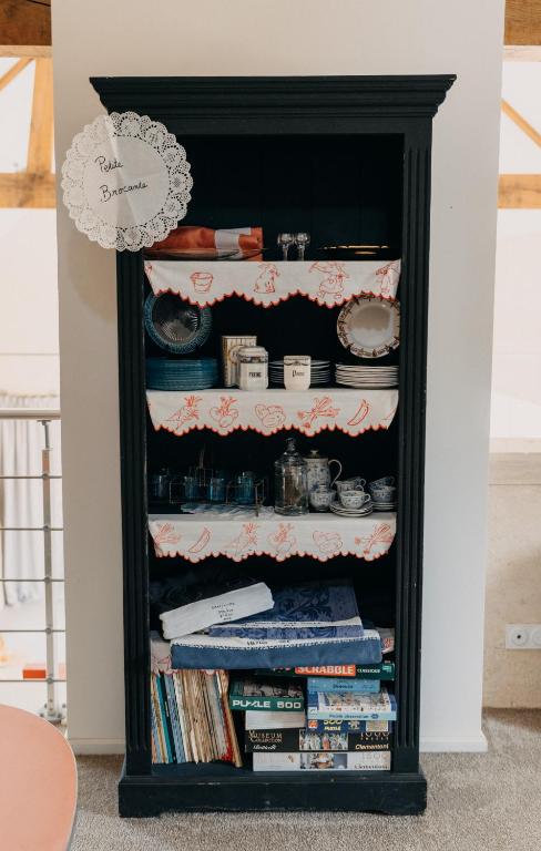 a black book shelf with dishes and books at Les Granges Pelloquin in Bernières-sur-Mer