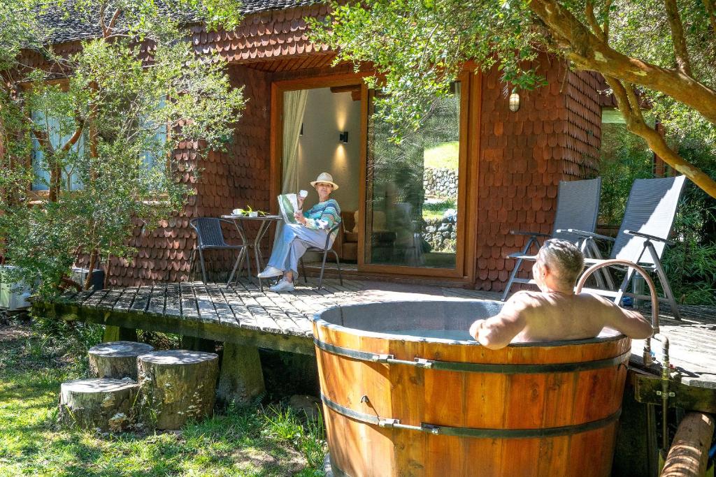 Un uomo seduto in una vasca da bagno in legno di barile di fronte a una casa di Hotel y Termas Huife a Termas De Huife