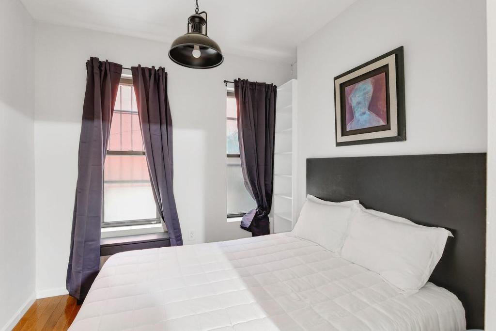 um quarto com uma cama branca e 2 janelas em Apartment 799: Hells Kitchen em Nova York