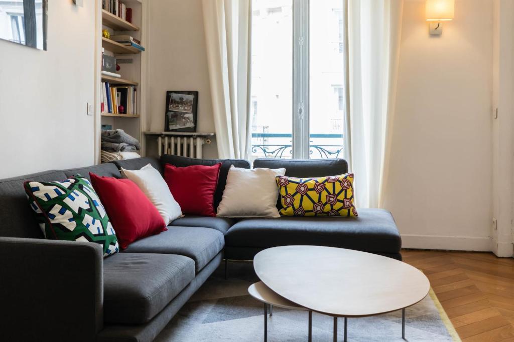 a living room with a blue couch with colorful pillows at Beautiful &amp; Bright Apartment Near Pigalle in Paris