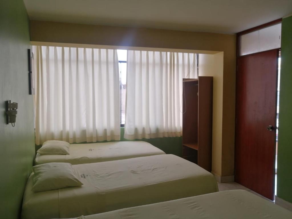 a bedroom with two beds and a window with curtains at Hostal Boulevard in Nazca