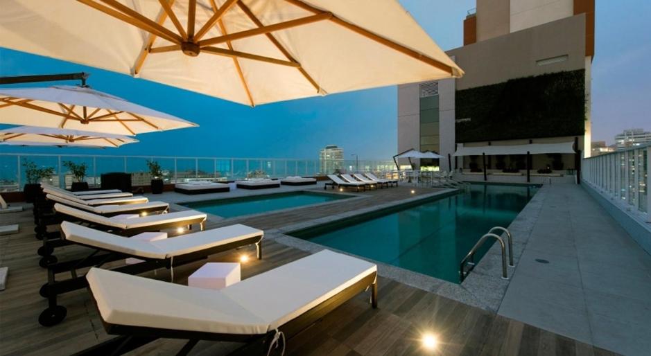 a swimming pool with chairs and umbrellas on a building at Residencial Legend in Santos