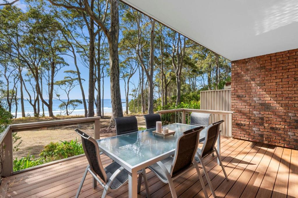 a glass table and chairs on a deck with the beach at Denhams Beach Waterfront in Surf Beach